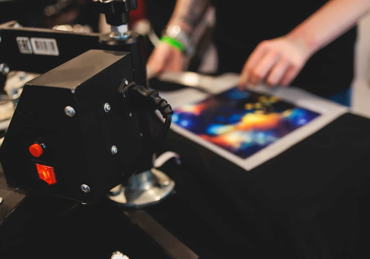 A person uses a heat press machine to apply a vibrant, abstract design onto a hoodie.